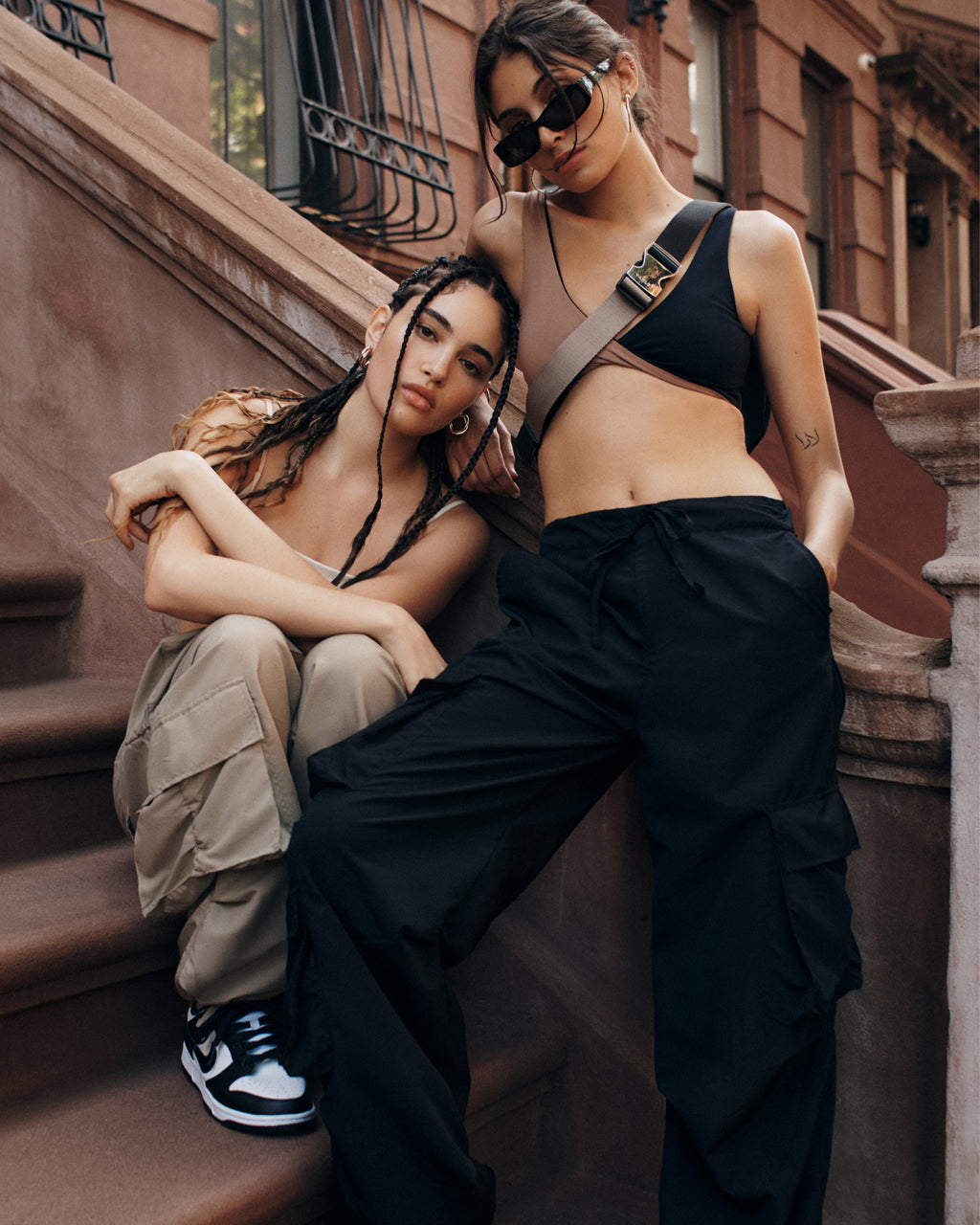 Two models sitting on the steps of a brownstone in New York wearing brown and black streetwear from Muv Activewear